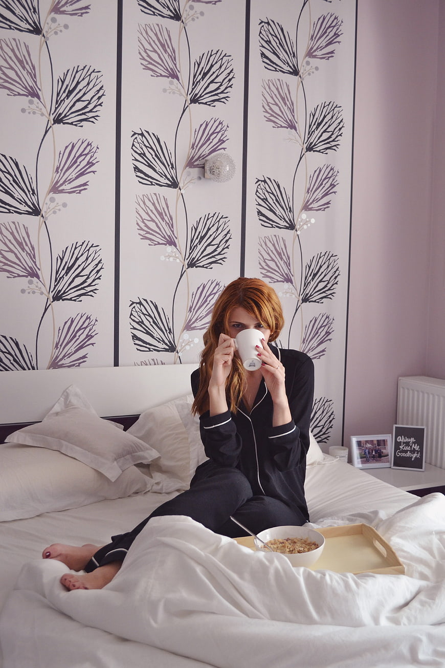 Woman in black pajamas enjoying breakfast in bed with coffee and cereal