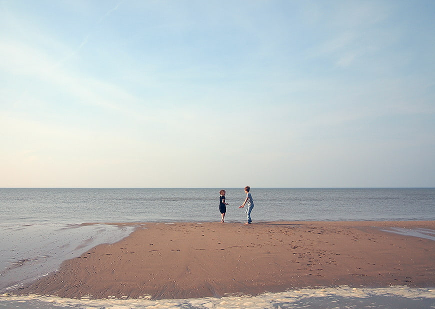 Two children playing on a sandy beach spit at low tide