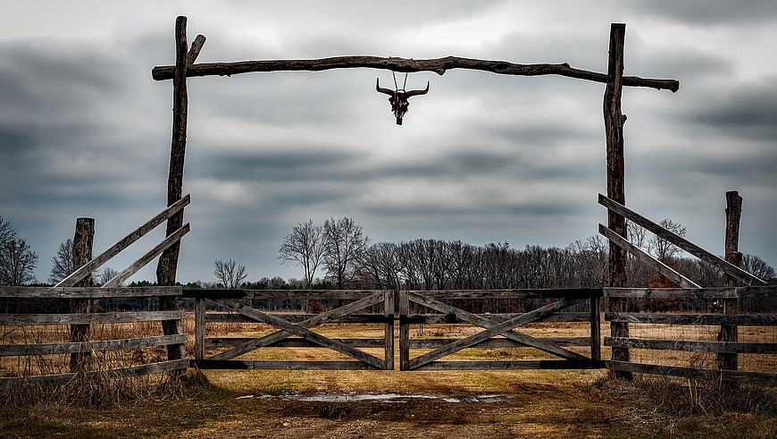 Rustic Ranch Gate with Hanging Bull Skull Under Cloudy Sky