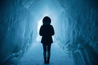Woman standing in blue ice cave tunnel looking at light