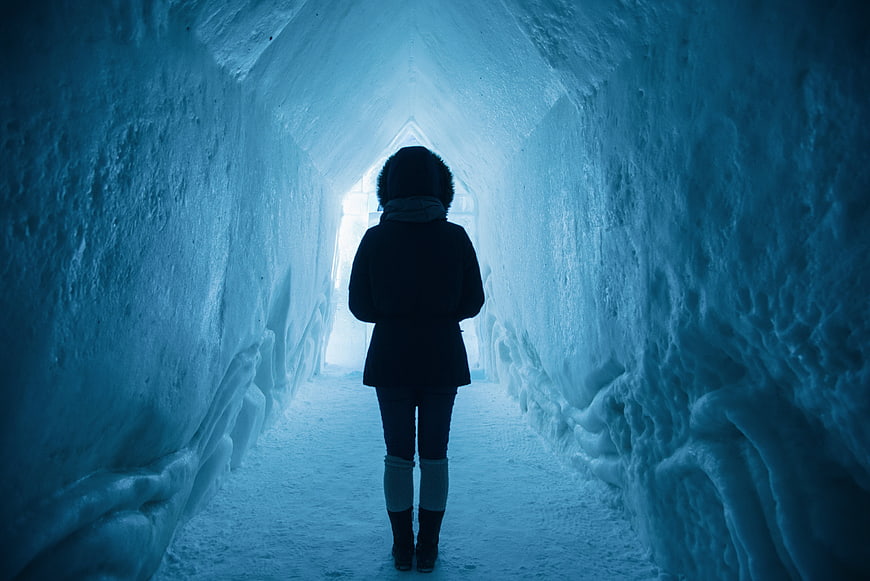 Woman standing in blue ice cave tunnel looking at light