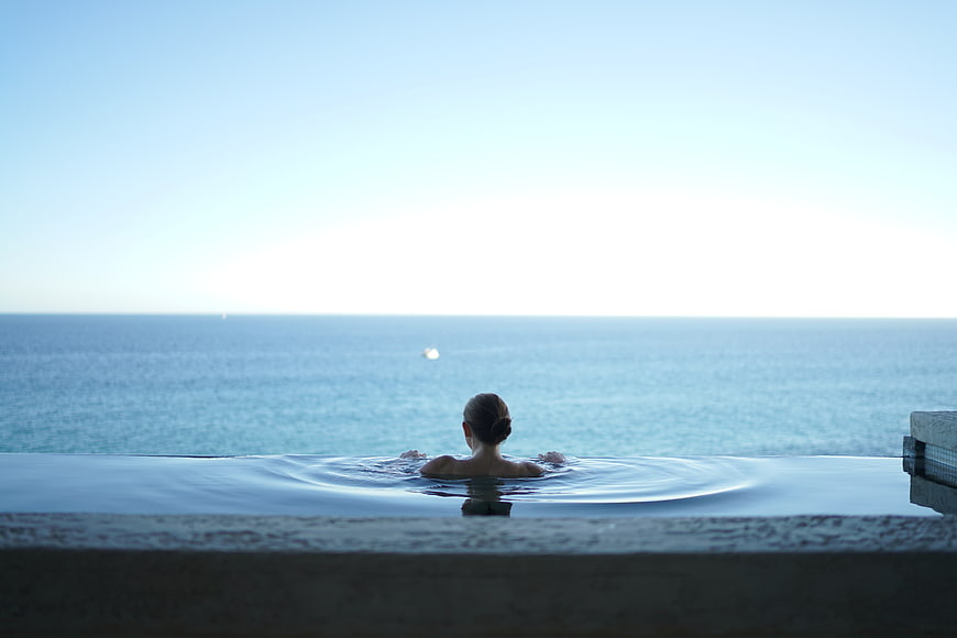 Woman relaxing in infinity pool overlooking calm ocean horizon