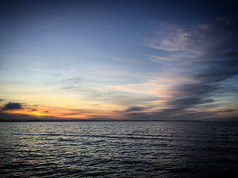 Serene Sunset Over Calm Ocean with Distant City Skyline