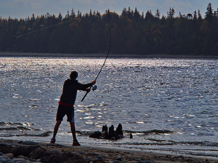 Silhouette of Boy Fishing on Rocky Shoreline at Sunset