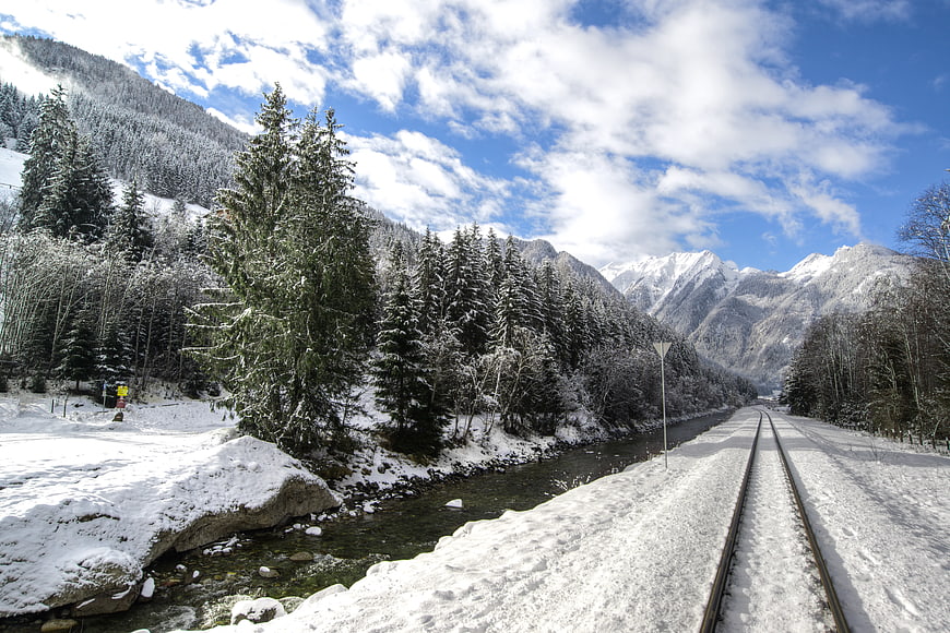 Snowy Railway Tracks Winding Through Alpine Forest and Mountains