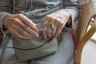 Close-up of elderly woman's hands holding reading glasses and purse