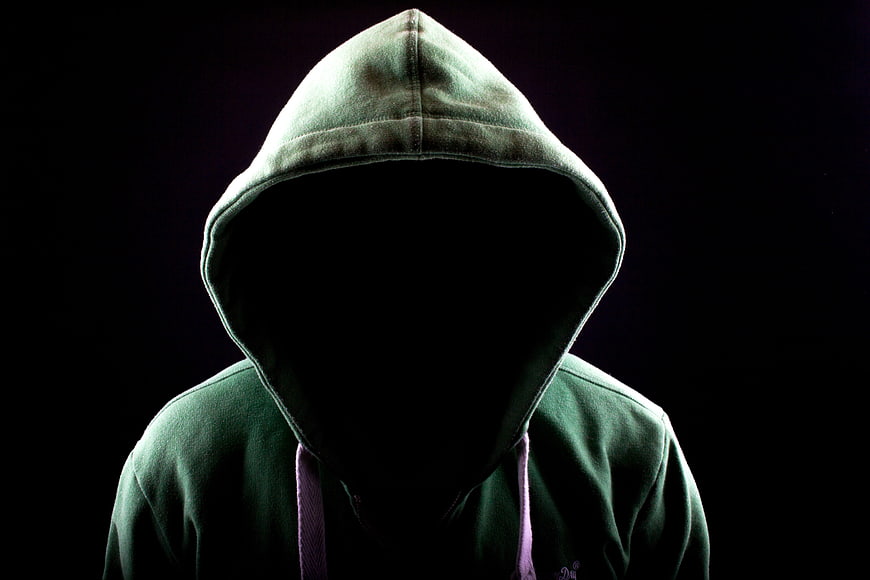 Anonymous figure in green hoodie with shadowed face