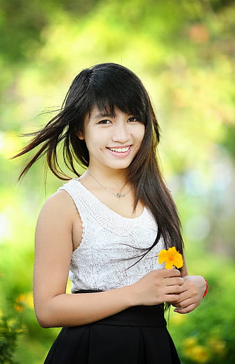 Smiling Young Woman Holding Yellow Flower in Park