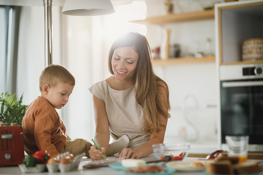 Happy mother and young son drawing together in bright kitchen