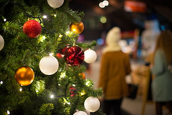 Close-up of Christmas tree with red and gold ornaments and blurred market background