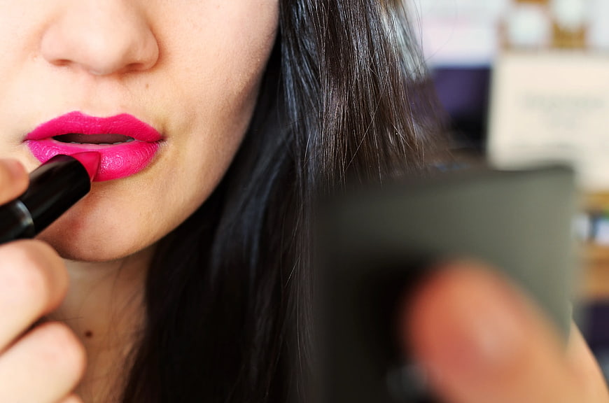 Close-up of woman applying bright pink lipstick