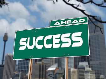 Green Success Ahead Road Sign Against Blurred City Skyline