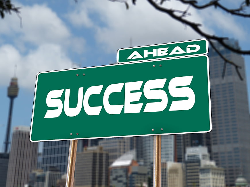 Green Success Ahead Road Sign Against Blurred City Skyline
