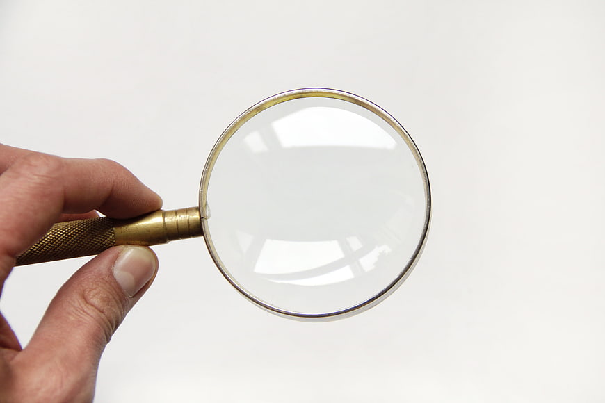 Hand holding brass magnifying glass on white background