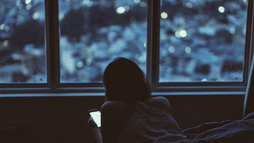 Woman in bed looking at phone by window at night
