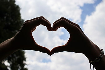 Silhouette of hands forming a heart shape against a cloudy blue sky