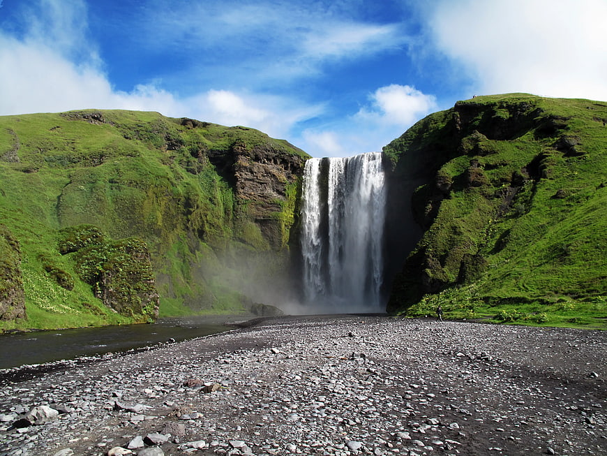 Skógafoss Waterfall in Iceland with Green Hills and Blue Sky