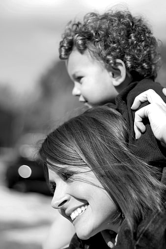 Black and white portrait of smiling mother carrying child on shoulders