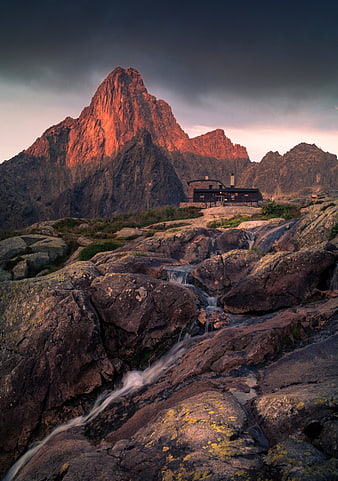 Dramatic mountain peak with alpine hut and rocky stream