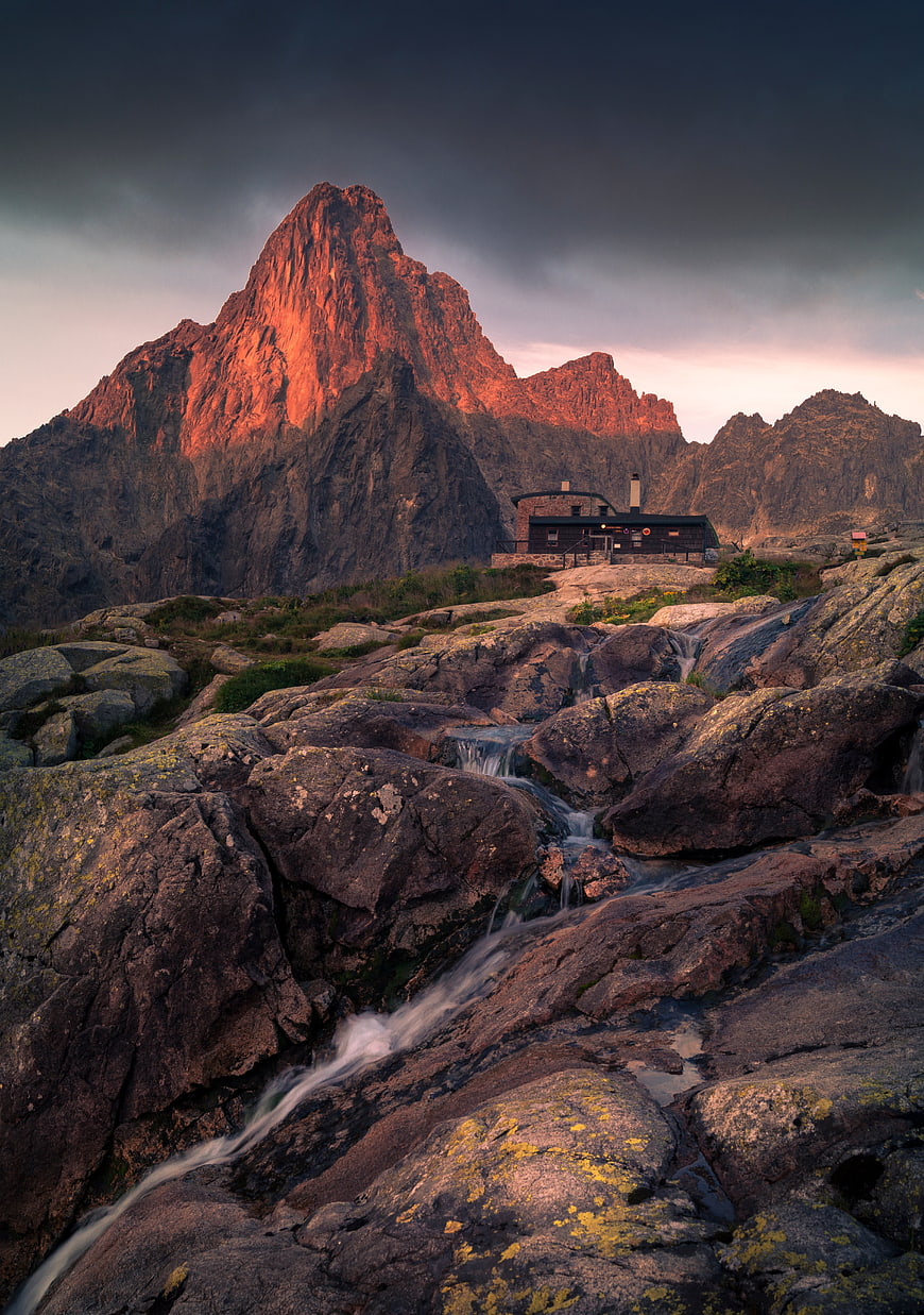 Dramatic mountain peak with alpine hut and rocky stream