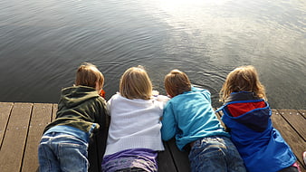 Four children lying on wooden dock looking at water