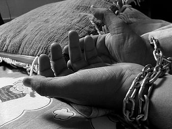 Black and white photo of hands bound by heavy metal chains