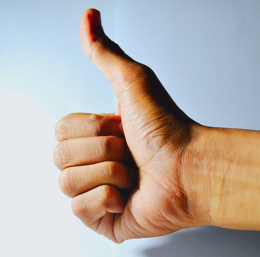 Close-up of hand giving thumbs up gesture against blue background