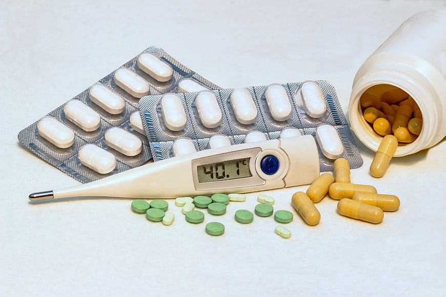 Digital thermometer showing high fever with pills and capsules