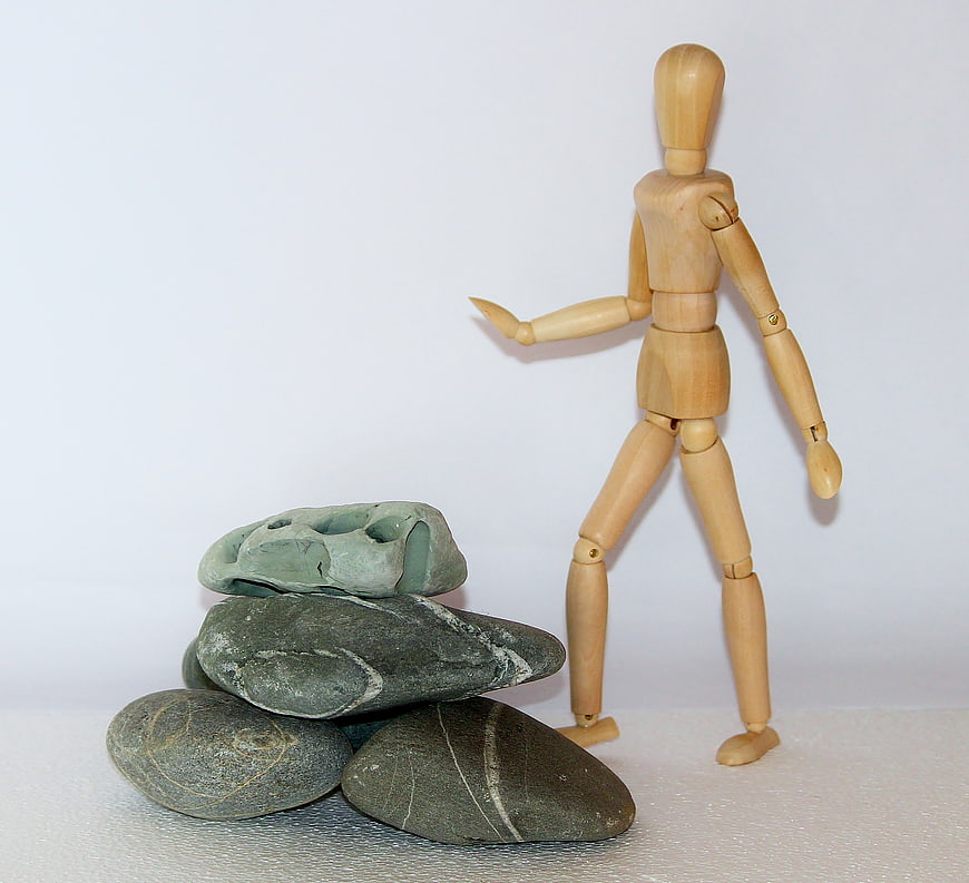 Wooden artist mannequin standing next to a stack of smooth gray stones