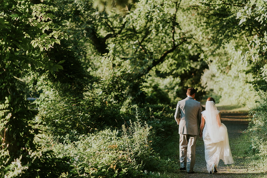 Bride and groom walking away on a sunlit forest path