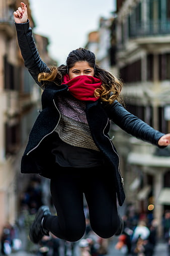 Happy woman jumping in city street with red scarf