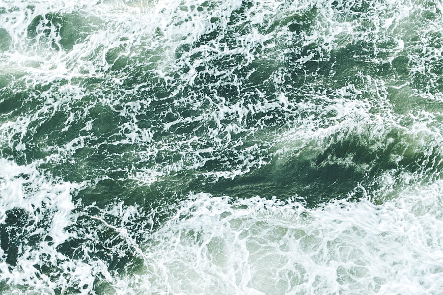 Aerial view of turbulent green ocean waves with white foam