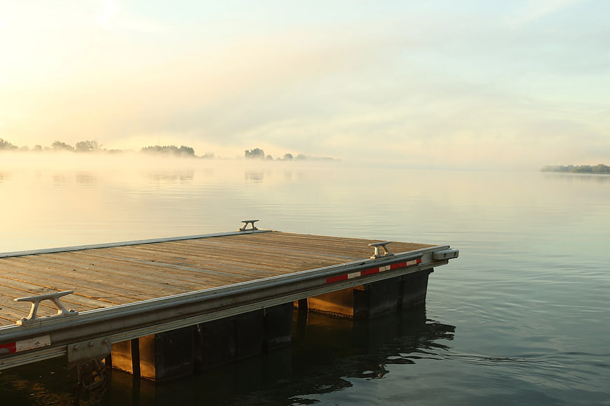 Misty wooden dock on calm lake at sunrise