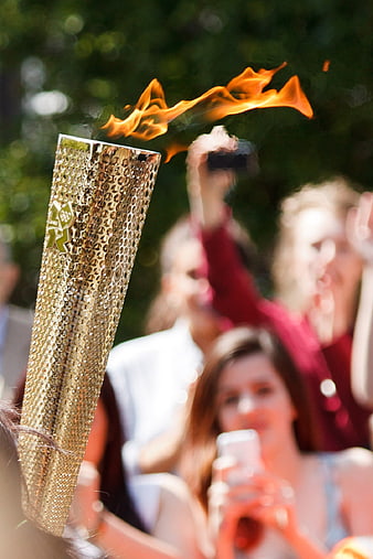 Gold Olympic Torch With Flame In Crowd