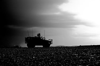 Silhouette of military armored vehicle on rocky terrain under stormy sky