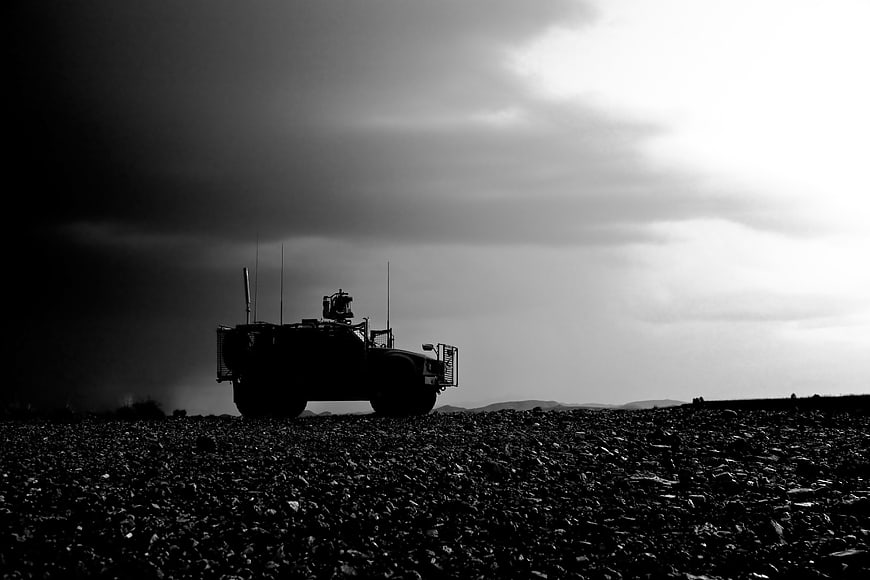 Silhouette of military armored vehicle on rocky terrain under stormy sky