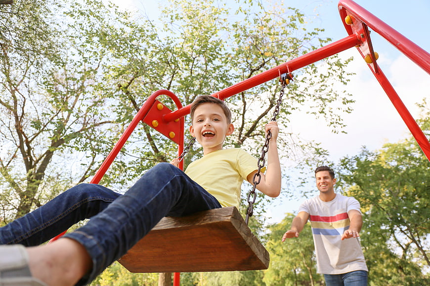 Happy Boy Swinging with Father in Park