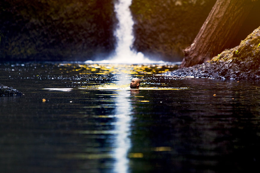 Man swimming in river with waterfall background