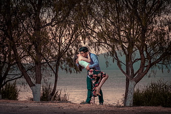 Romantic Couple Kissing Under Trees by Lake at Sunset
