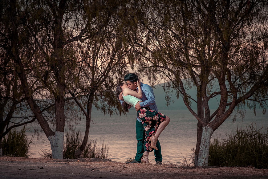 Romantic Couple Kissing Under Trees by Lake at Sunset