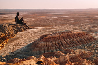 Man sitting on cliff edge overlooking vast desert canyon landscape
