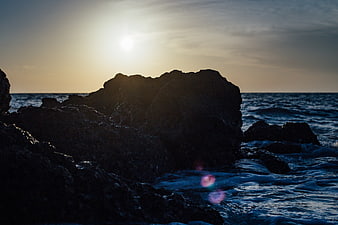Silhouette of dark rocks against ocean sunset waves