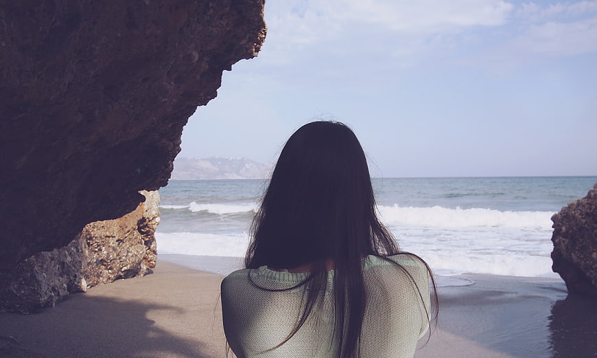 Woman with long hair looking at ocean from rocky cave