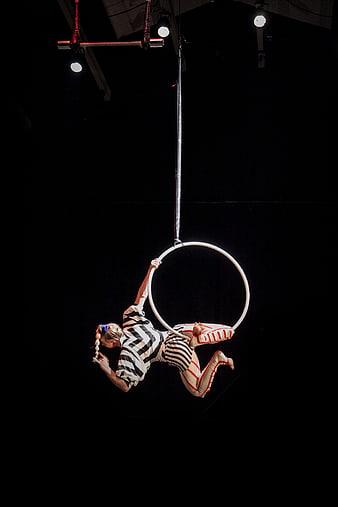 Female aerial hoop performer suspended in a dark circus arena