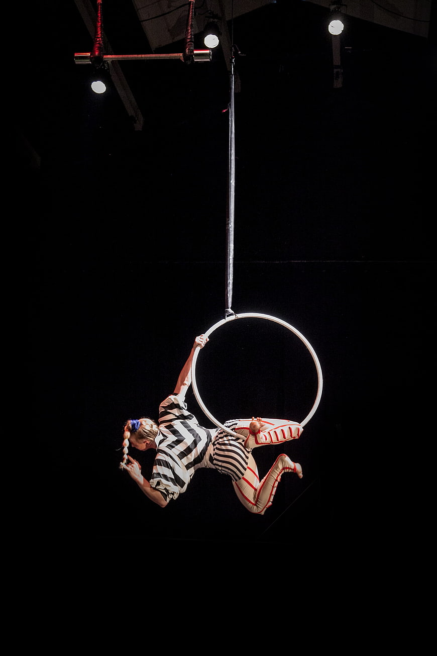 Female aerial hoop performer suspended in a dark circus arena