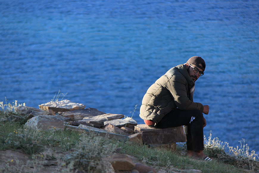 Man sitting on stone bench by blue lake
