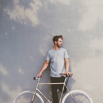Man with bicycle leaning against gray wall