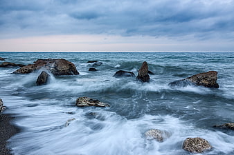 Dramatic long exposure ocean waves crashing on rocky shore