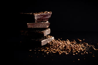 Stacked dark chocolate pieces with shavings on black background