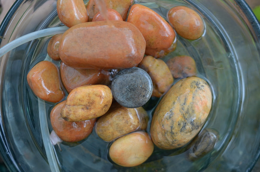 Top view of smooth orange stones in a glass water fountain